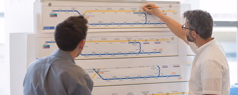 Two male co-workers planning train routes on a transit map