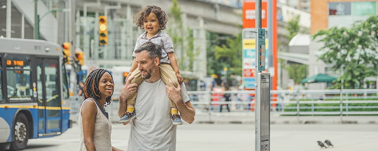 A family of three standing by a bus stop waiting for the bus