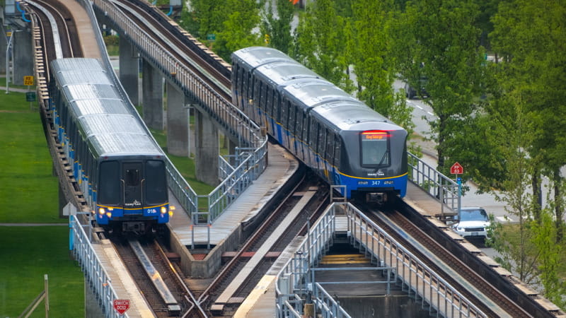 Two SkyTrains on tracks surrounded by greenery.