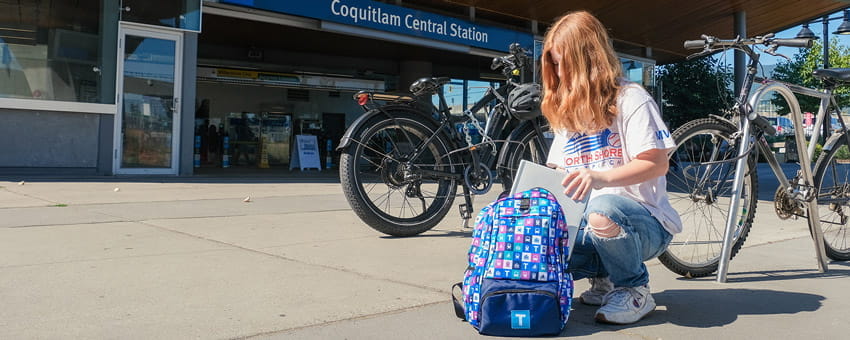 A transit user putting their laptop into their backpack in front of Coquitlam Central Station