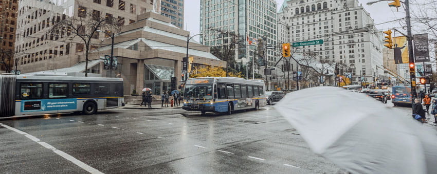 Two buses downtown during rainy weather with a grey umbrella in the foreground