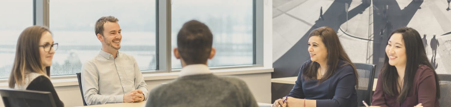 Five employees sitting around each other in a well-lit meeting room